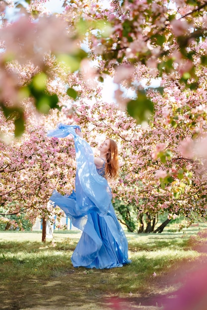 Юная сказочная девушка в нежно-голубом платье отбрасывает ткань на фоне розового платья ...