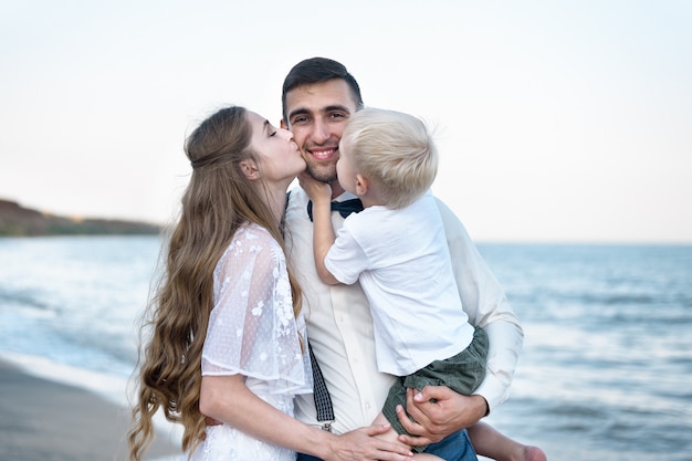 Young family on the beach. Wife and son kiss daddy. Beautiful couple on vacation with the child