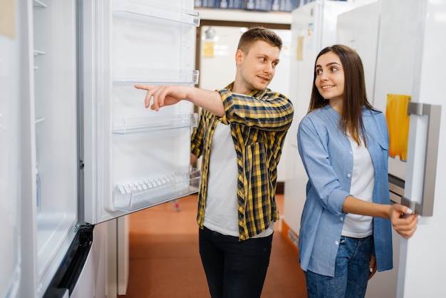 Young family couple choosing refrigerator in electronics store. Man and woman buying home electrical appliances in market