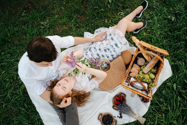 A young family couple is resting on a picnic lying on a light blanket on the lawn in the field a romantic walk for the husband and wife in the park