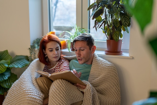Young family couple man and woman discussing new book while reading together at home