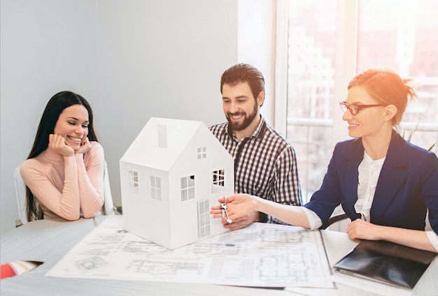 Coppia giovane famiglia acquisto affitto proprietà immobiliare. agente che consulta l'uomo e la donna. firma del contratto per l'acquisto di casa o appartamento o appartamenti. tiene in mano un modello della casa