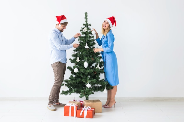 Young family couple in santa hats decorating the christmas tree