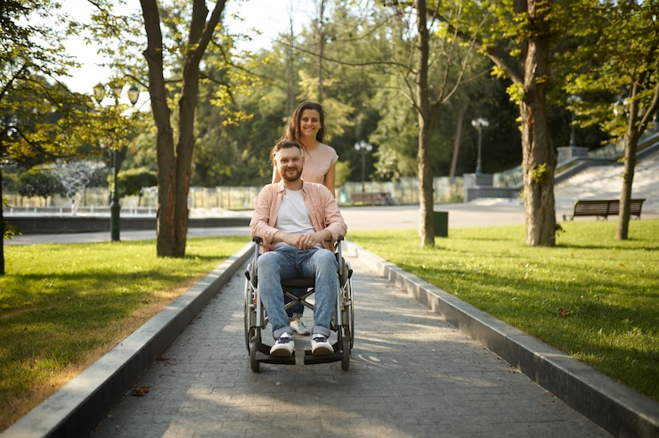 Photo young family couple with wheelchair walking in the park. paralyzed people and disability, care for a disabled man. husband and wife overcome difficulties together, warm relationships
