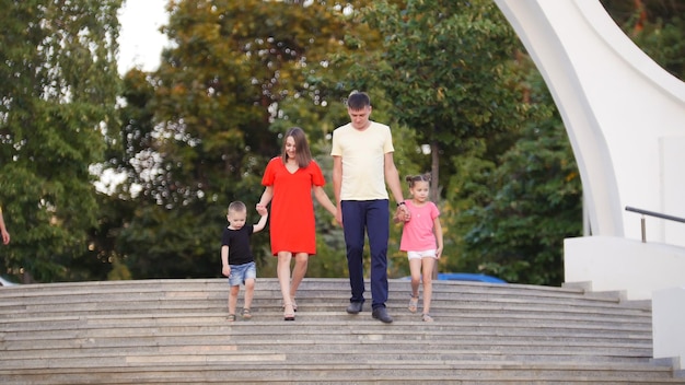 Young family of four dad mom daughter and son down the stairs in the park talking