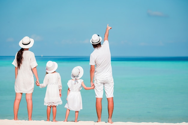 Young family of four in white on tropical beach. PArent with two little kids looking at the sea