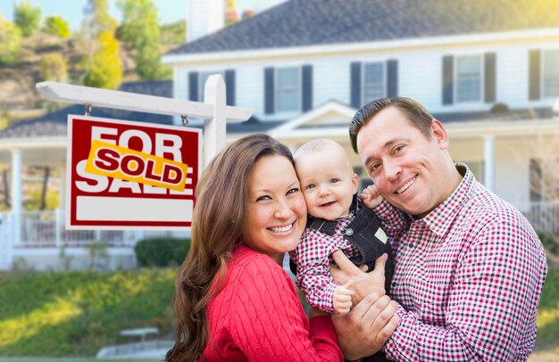 Photo young family in front of for sale sign and house