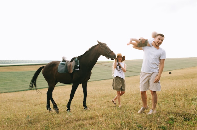 A young family have a fun in the field. Parents and child with a horse