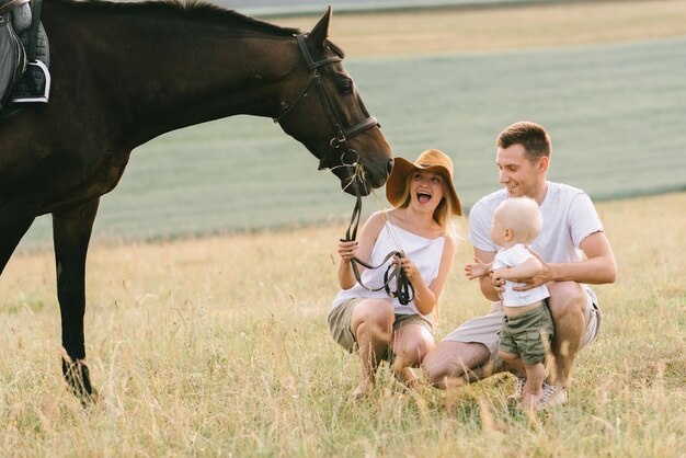 Una giovane famiglia si diverte sul campo. genitori e bambino con un cavallo