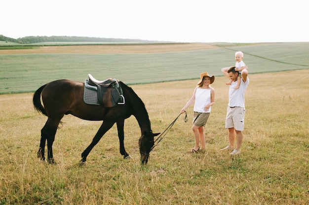 A young family have a fun in the field. Parents and child with a horse