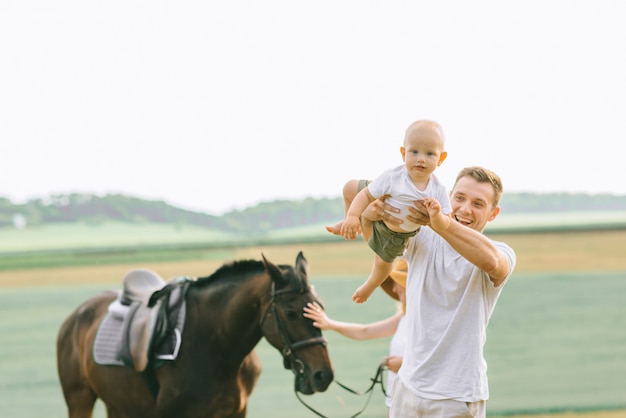 A young family have fun in the field. Parents and child with a horse