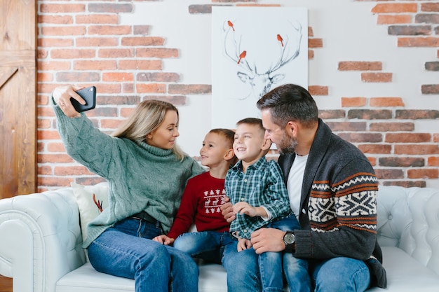 Молодая семья весело разговаривает по видеозвонку по мобильному телефону, радуясь и улыбаясь, муж жена и ваши парни братья поздравляют друзей с Новым годом и рождественскими праздниками.