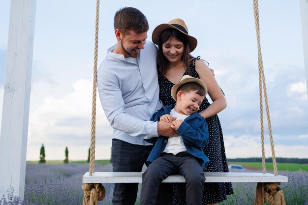 Young family is playing with their son who is sitting on a swing in a lavender field