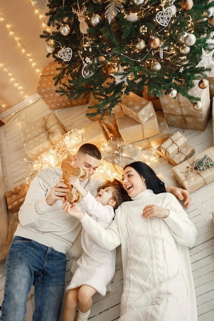 Young family laying near Christmas tree and celebrating together