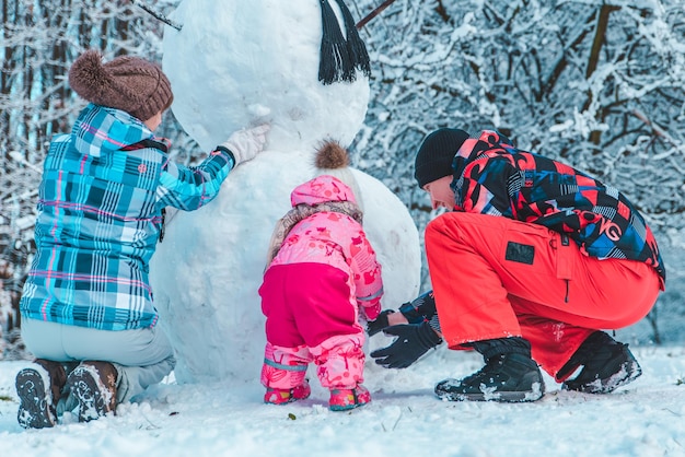 冬の都市公園で遊んでいる若い家族。雪だるまを作る。クリスマスが来ています