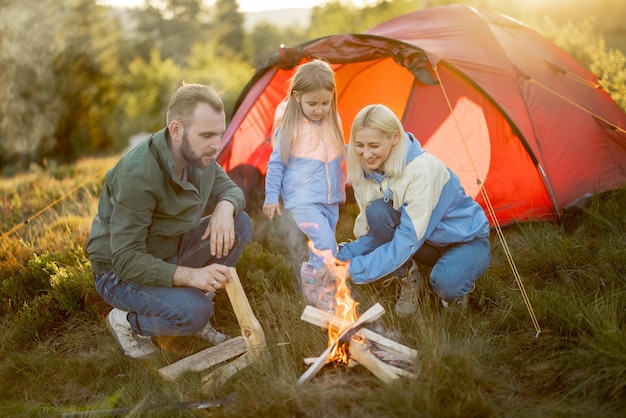 若い家族は自然のテントの近くのキャンプファイヤーのそばに座っています