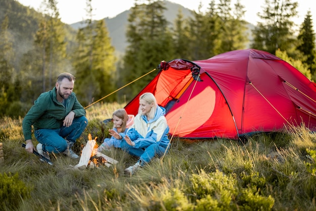 Young family sit by the campfire near tent on nature