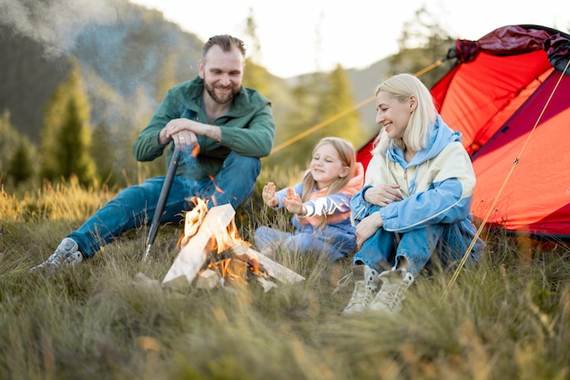 La giovane famiglia si siede vicino al fuoco vicino alla tenda sulla natura