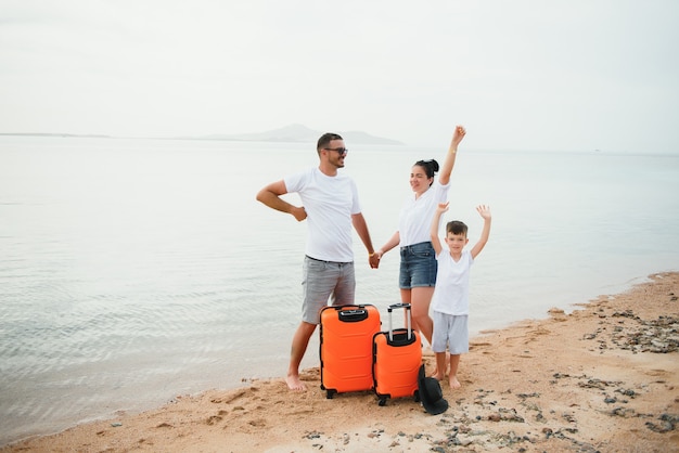 Young family and son with luggage on tropical white beach