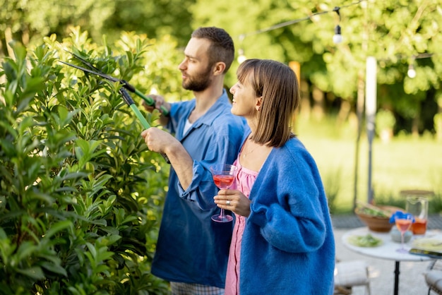 若い家族は彼らのカントリーハウスの裏庭で茂みを剪定する夏の時間を過ごします