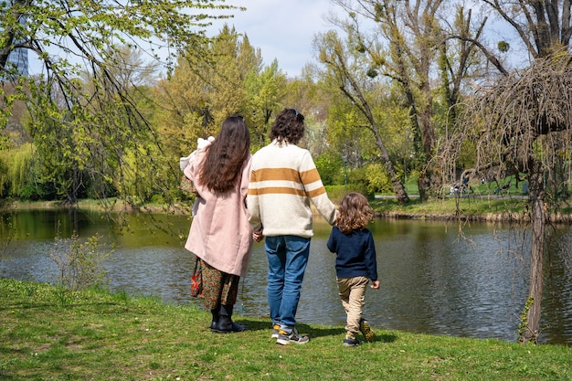 Young family staying in a park and holding hands, turned backs into the camera 