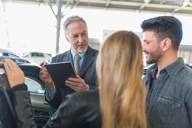 Foto giovane famiglia che parla con il venditore e sceglie la sua nuova auto in uno showroom