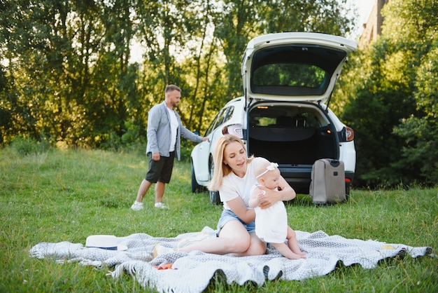 Young family three people in white clothes have picnic. Beautiful parents and daughter travel by car during summer vacation.