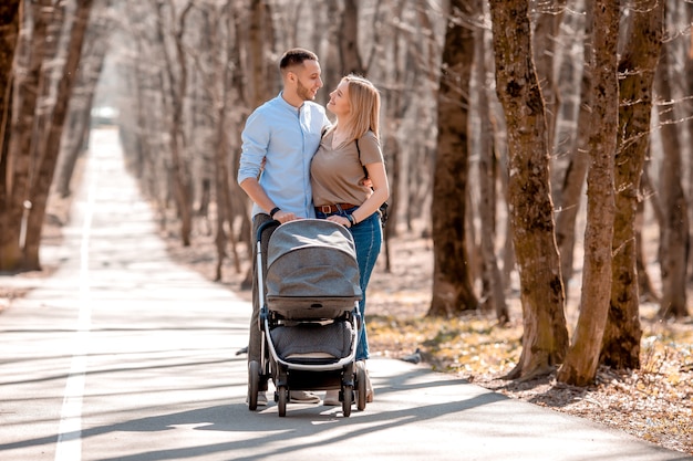Молодая семья прогулка в парке весной с малышом в коляске. Счастливые родители