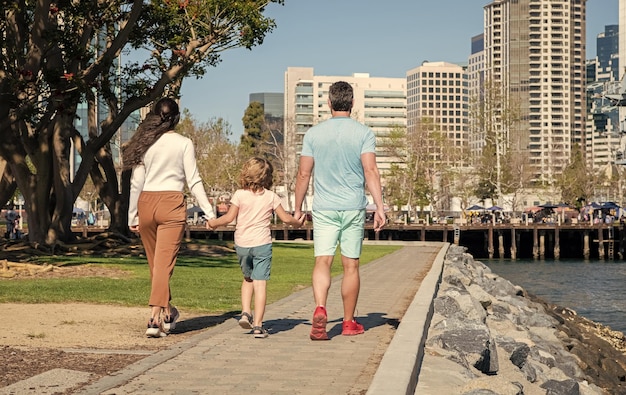 Молодая семья гуляет в парке с сыном, вид сзади родителей