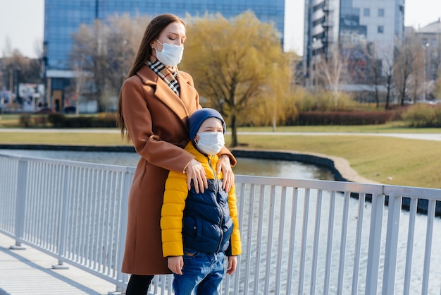 検疫とパンデミックの最中、晴れた日に若い家族が歩いて新鮮な空気を吸い込みます。人々の顔のマスク。