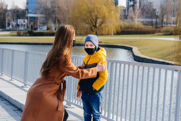 検疫とパンデミックの最中、晴れた日に若い家族が歩いて新鮮な空気を吸い込みます。人々の顔のマスク。