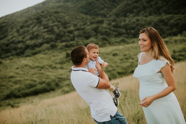 Young family with cute little boy having fun outdoors in the summer field