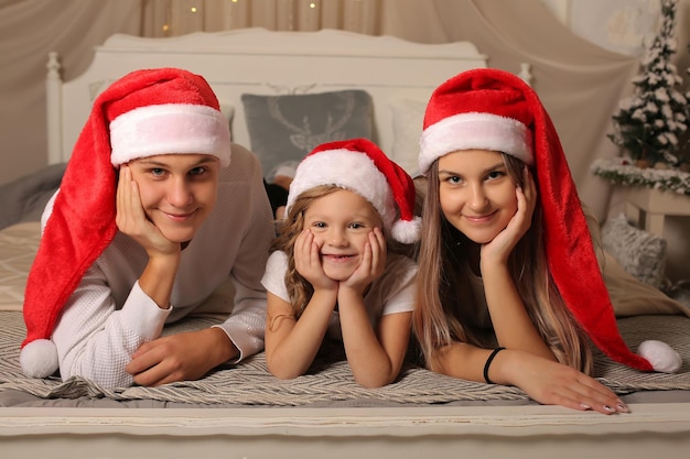 A young family with a little daughter in santa claus hats are lying on the bed at home christmas