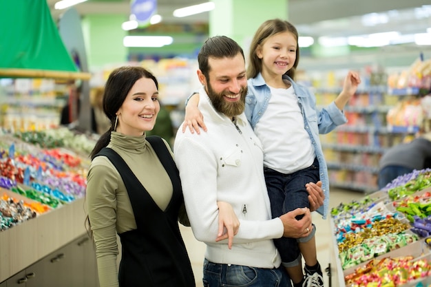 A young family with a little girl choose candy and chocolate in a large store, supermarket.