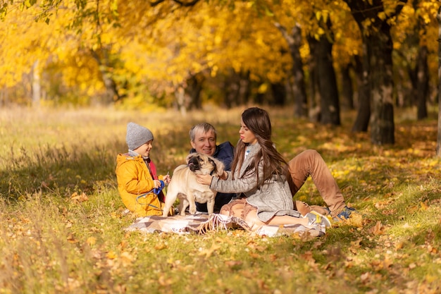 Молодая семья с маленьким ребенком и собакой вместе гуляет в осеннем парке.