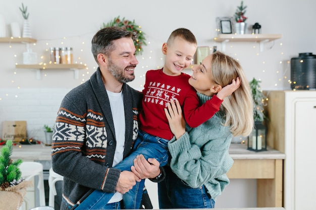 Photo a young family with a son in the kitchen rejoice in the holidays, a husband and wife and a little boy have fun together hugging and playing on new year's and christmas holidays