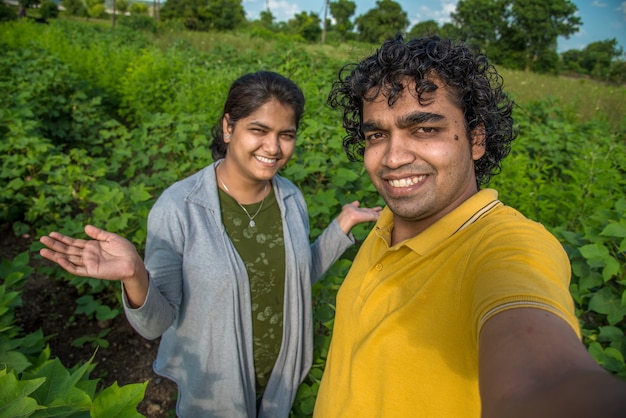 Coppia di giovani agricoltori prendendo un selfie con uno smartphone o una fotocamera nella fattoria di cotone.