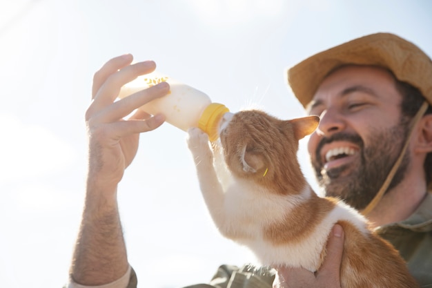 Young farmer feeding his cat milk from a bottle at the farm