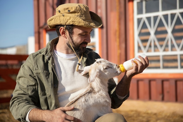 Foto giovane agricoltore che alimenta il suo latte di capra da una bottiglia alla fattoria