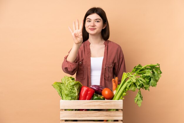 Молодой фермер девушка со свежесобранными овощами в коробке счастливы и считает четыре пальца
