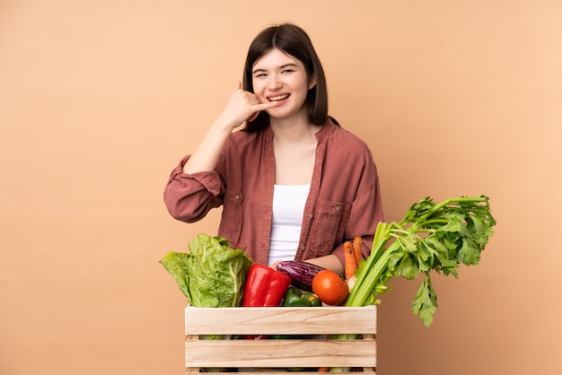 Ragazza giovane agricoltore con verdure appena raccolte in un gesto del telefono di fabbricazione di scatola