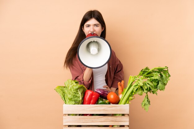 Foto ragazza giovane agricoltore con verdure appena raccolte in una scatola che grida tramite un megafono