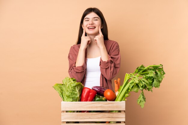 Young farmer girl with freshly picked vegetables in a box smiling with a happy and pleasant expression