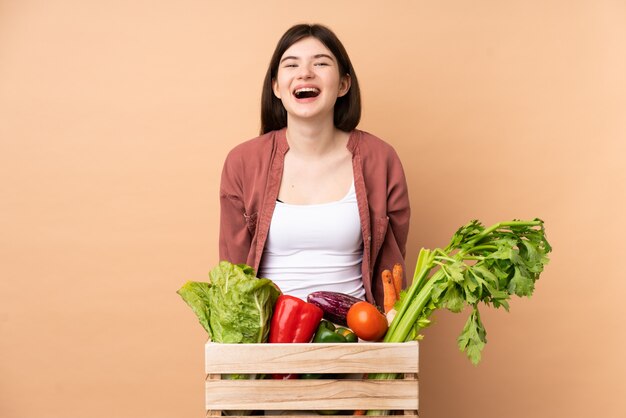 驚きの表情を持つボックスで摘みたての野菜を持つ若い農家の少女