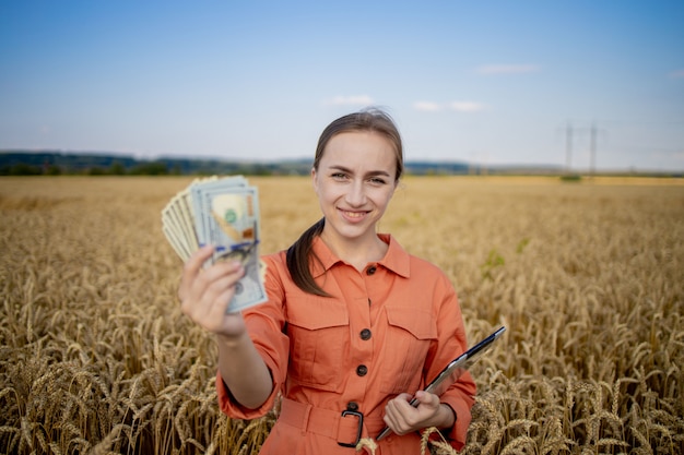 Young farmer holding dollars in golden wheat field