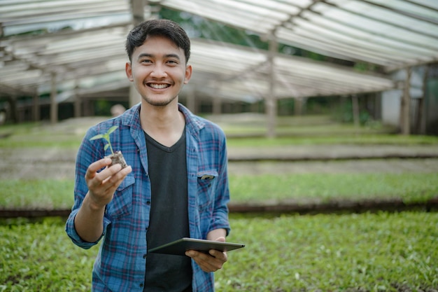 写真 カメラデジタル農業写真の概念を見て種子植物とタブレットを保持している若い農家