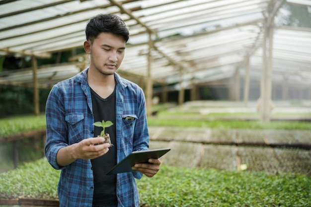 写真 カメラデジタル農業写真の概念を見て種子植物とタブレットを保持している若い農家