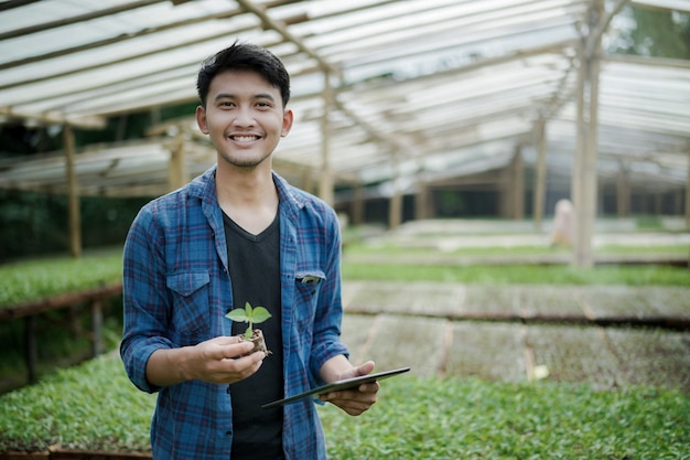 young farmer holding seed plant and tablet looking at the camera digital farming photo concept