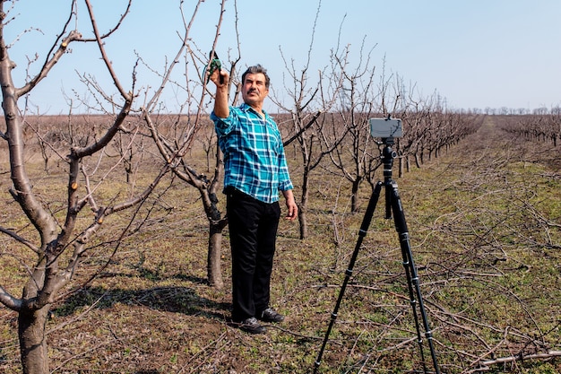 Giovane agricoltore potatura di alberi da frutto in primavera. blogger influencer che registra video blog