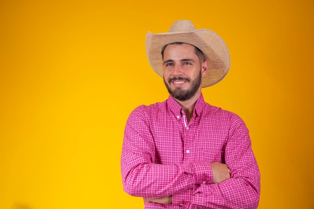 Young farmer with plaid shirt and arms crossed on yellow background Farmer dressed for the June party